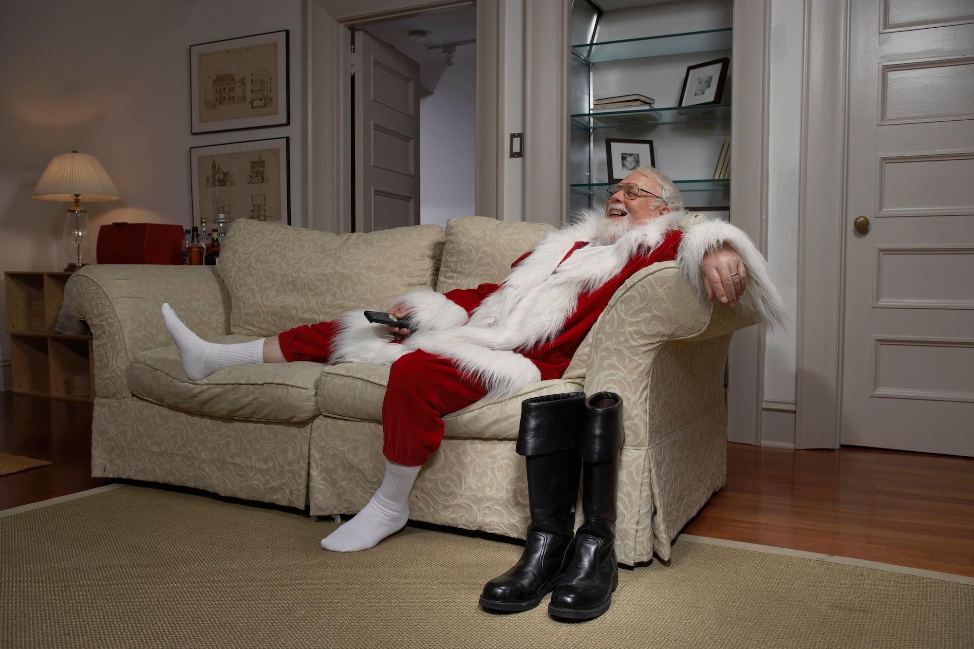 Der Weihnachtsmann entspannt sich auf dem Sofa und hält die Fernbedienung in der Hand
