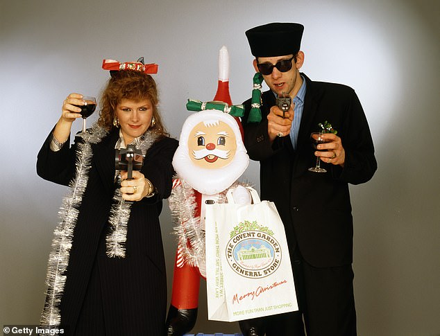 Die Sänger Kirsty MacColl (1959–2000) und Shane MacGowan (1957–2023) mit Spielzeugpistolen und einem aufblasbaren Weihnachtsmann in einem festlichen Szenario, etwa 1987. 1987 arbeiteten die beiden am Weihnachtslied „Fairytale of New York“ der Pogues zusammen
