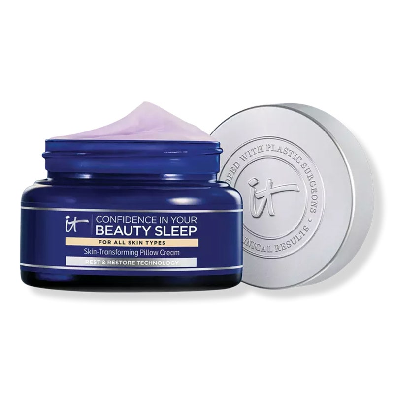 IT Cosmetics Confidence in Your Beauty Sleep Night Cream: Ein dunkelblaues Glas gefüllt mit lavendelfarbener Gesichtscreme neben einem silbernen Deckel auf weißem Hintergrund