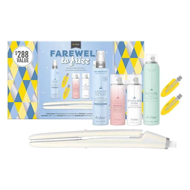 Drybar Farewell to Frizz Set: Ein weißes Glätteisen, vier verschiedenfarbige Flaschen Haarpflegemittel und zwei gelbe Haarspangen sowie eine mehrfarbige Geschenkbox auf weißem Hintergrund