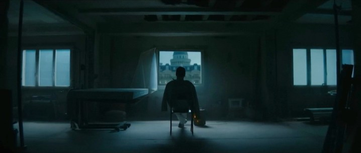 A man sits in front of a window in The Killer.