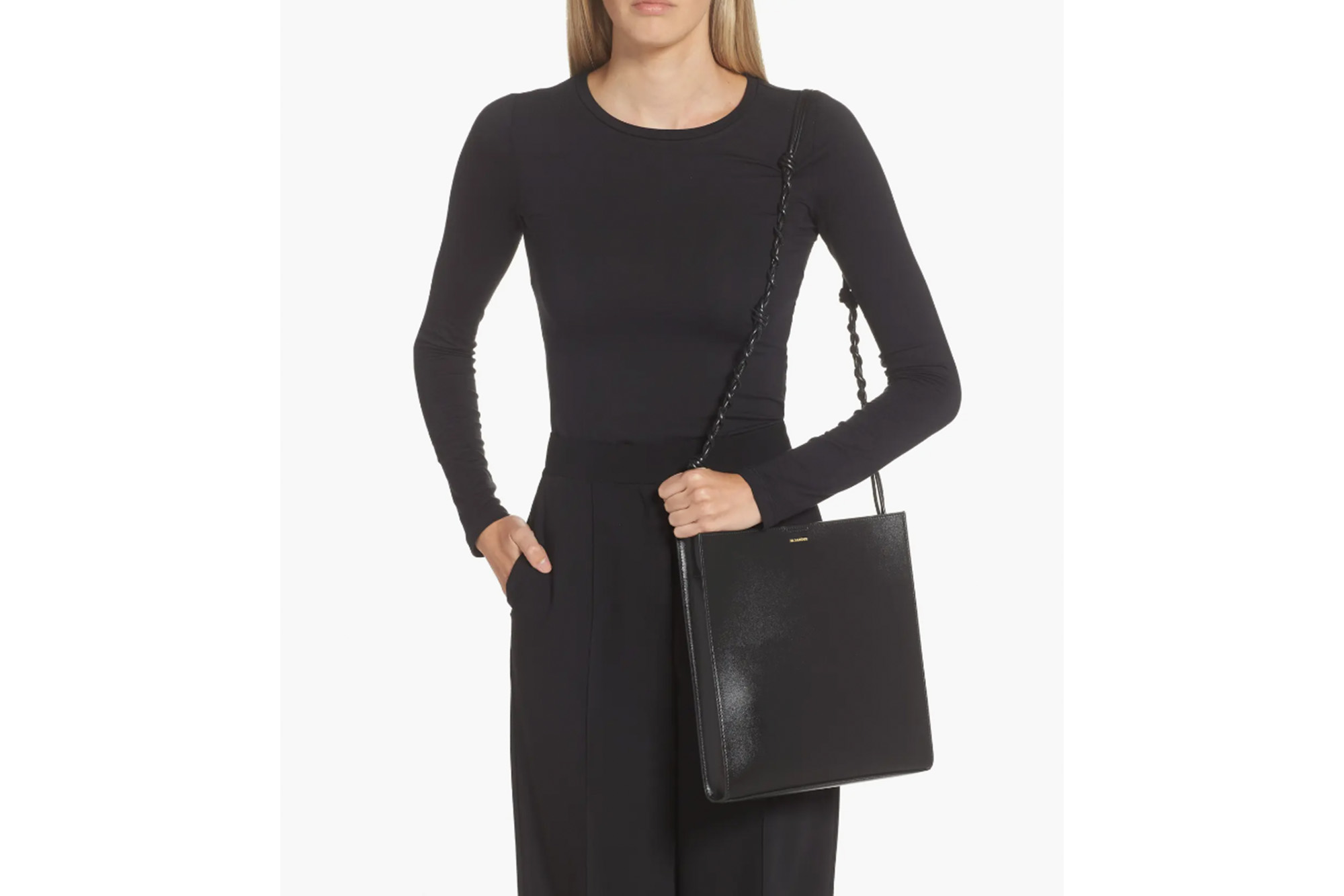 Ein Model in einem schwarzen Outfit mit passender Handtasche