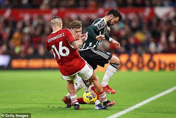 NOTTINGHAM, ENGLAND - DECEMBER 30: Bruno Fernandes of Manchester United is challenged by Ryan Yates and Nicolas Dominguez of Nottingham Forest during the Premier League match between Nottingham Forest and Manchester United at City Ground on December 30, 2023 in Nottingham, England. (Photo by Catherine Ivill/Getty Images)