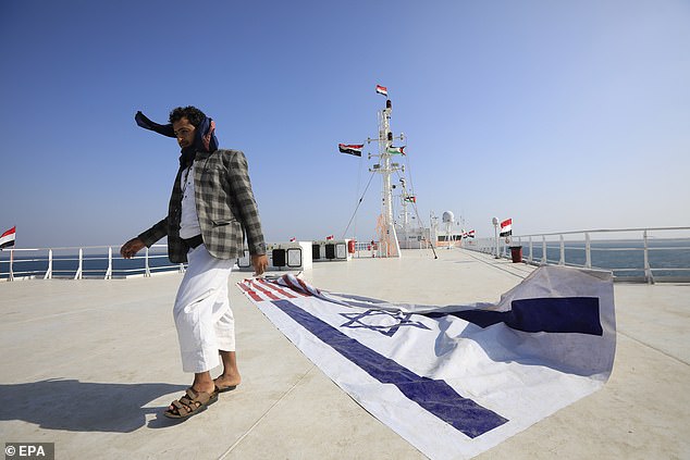 Ein Jemenit passiert ein Banner mit der israelischen und US-amerikanischen Flagge an Deck des Frachtschiffs Galaxy Leader, das am 5. Dezember von den Houthis vor der Küste des Hafens Al-Salif am Roten Meer in der Provinz Hodeidah, Jemen, beschlagnahmt wurde