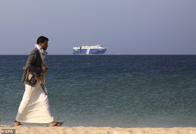 Ein bewaffneter Houthi-Kämpfer läuft am 5. Dezember mit dem Frachtschiff Galaxy Leader im Hintergrund durch den Strand, das von den Houthi vor der Küste des Hafens von Al-Salif beschlagnahmt wurde