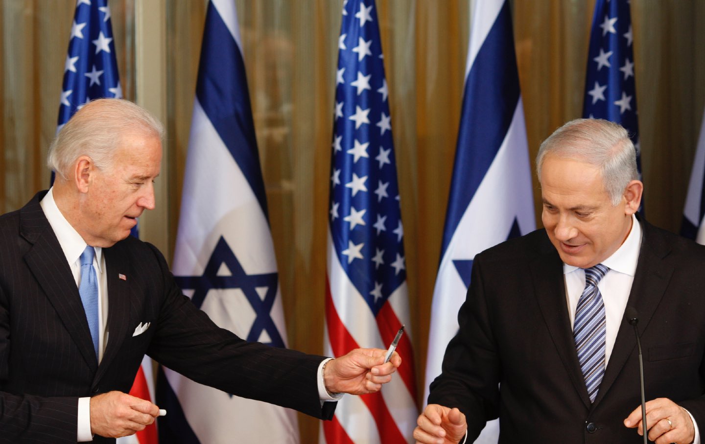 Biden gibt Netanjahu einen Stift.  Im Hintergrund sind die Flaggen der USA und Israels zu sehen