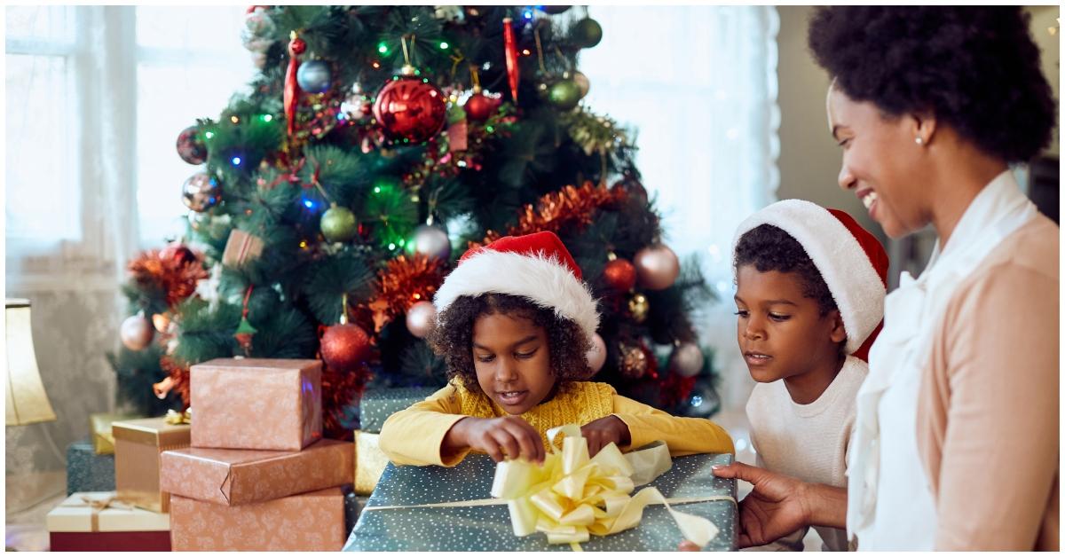(lr): Kinder öffnen ein Geschenk, während eine Frau ihnen zusieht