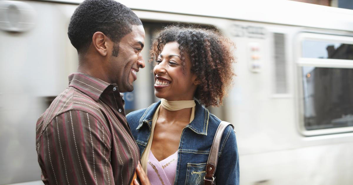 Ein junges Paar lächelt einander an, während es auf dem Bahnsteig wartet.