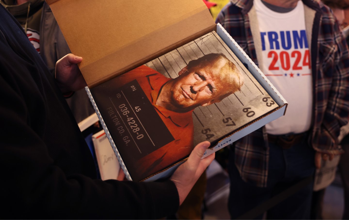 Ein Unterstützer hält einen Druck mit dem Fahndungsfoto von Donald Trump in der Hand, während er darauf wartet, dass er am 2. Dezember 2023 in der Whiskey River Bar in Ankeny, Iowa, ankommt.