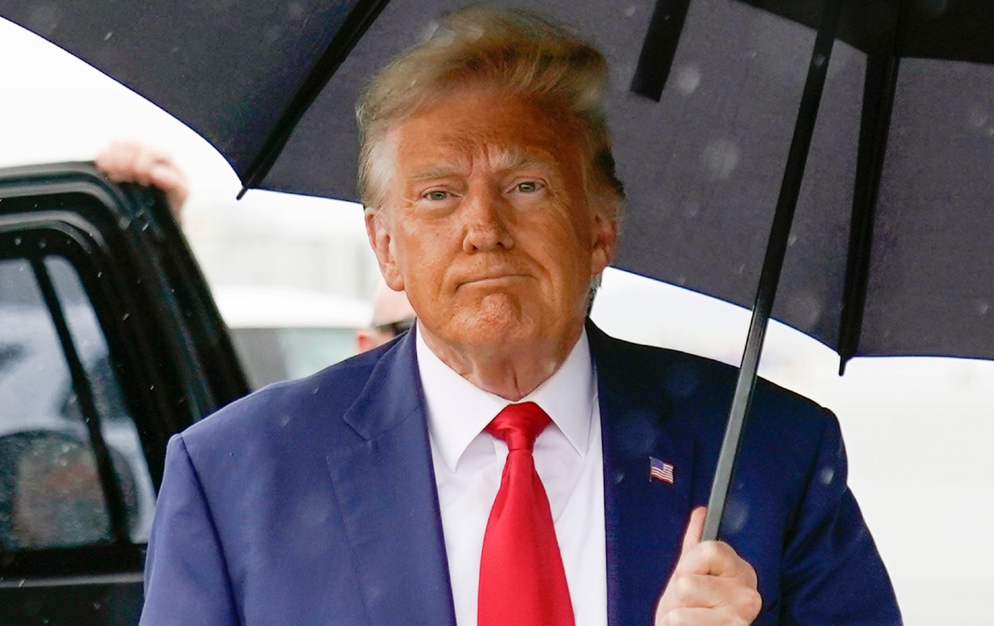 Trump hält einen Regenschirm in der Hand und geht zum Flugzeug