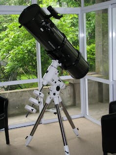 Ein großes schwarzes Teleskop auf einer weißen Halterung, das auf einer Veranda steht