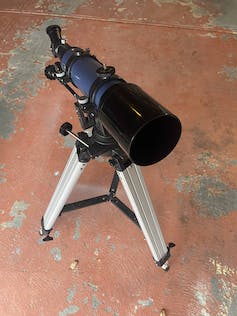 Ein kleines Teleskop, das auf einer einfachen Halterung auf einem Betonboden sitzt