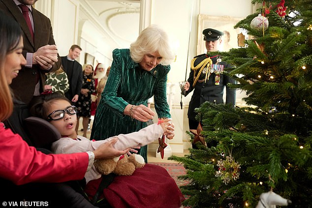 The Queen helps a child as they decorate a Christmas tree together at Clarence House