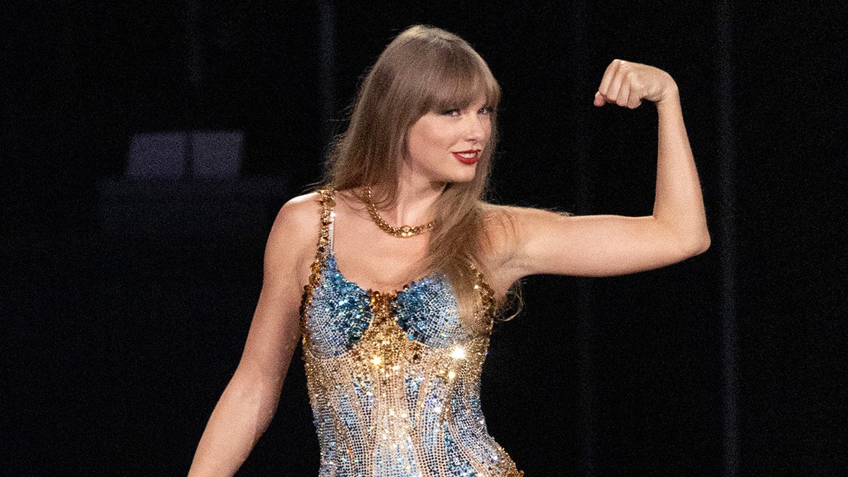 Taylor Swift lächelt mit erhobener Faust und trägt einen funkelnden Body