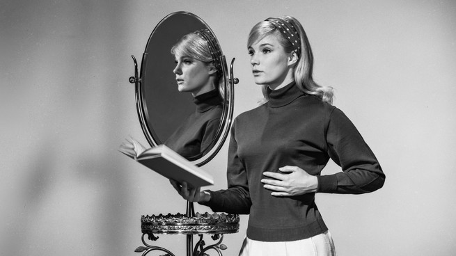 Ein Vintage-Schwarzweißfoto einer Frau, die ein Buch vor einem Spiegel hält