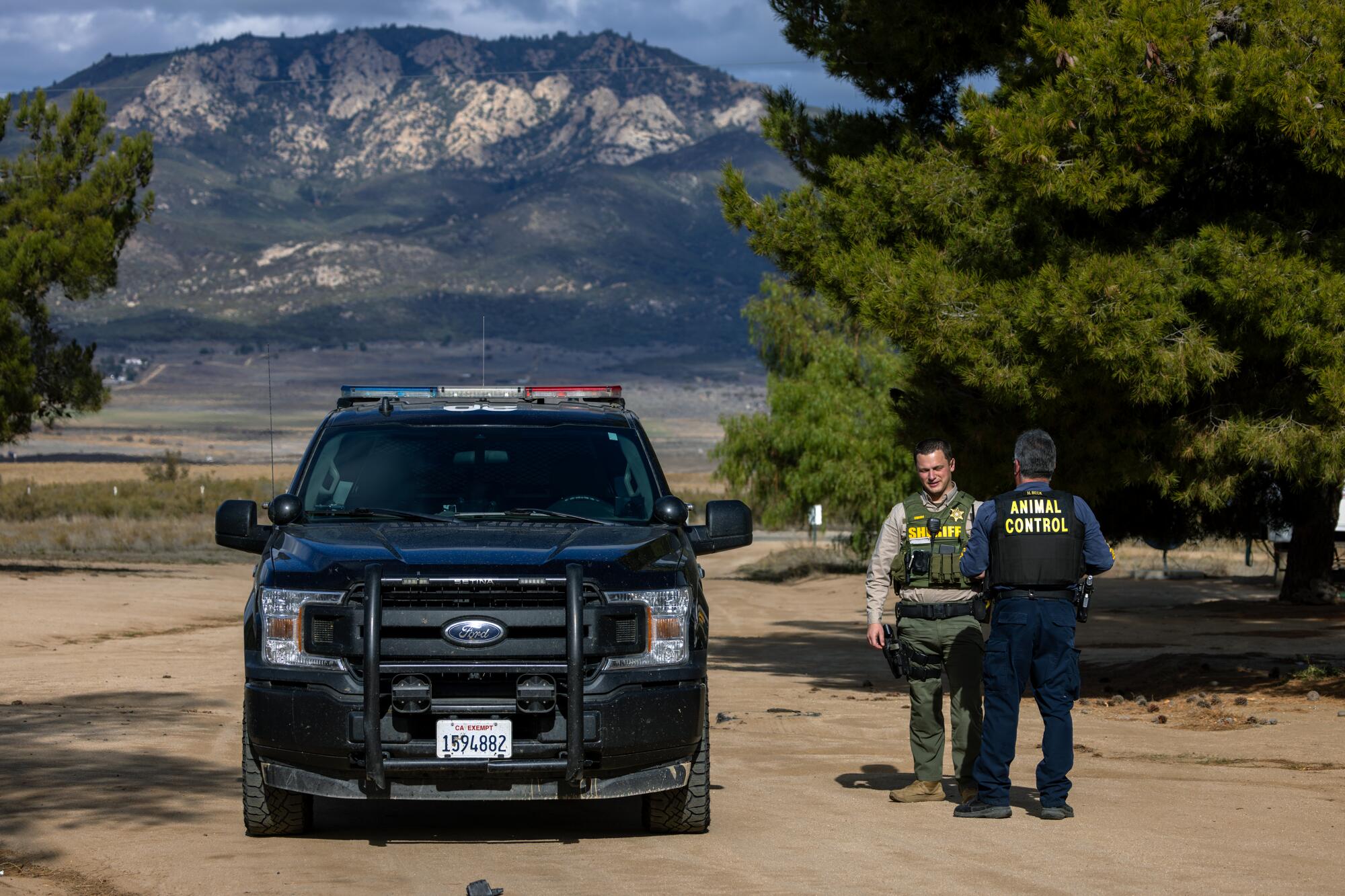 Ein Tierschutzbeamter und ein Stellvertreter des Sheriffs stehen neben einem Streifenwagen, während im Hintergrund ein Berg aufsteigt.