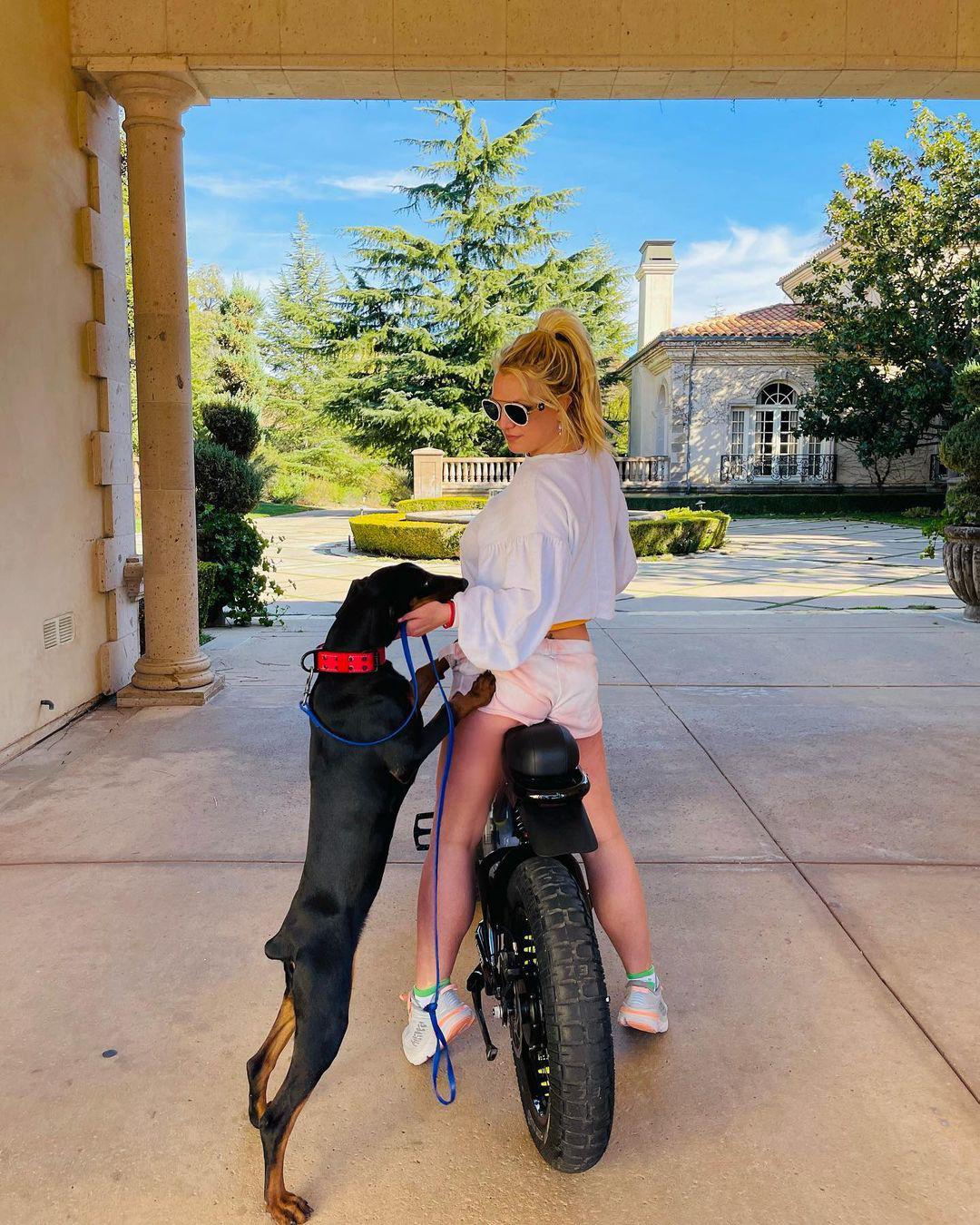 Britney Spears auf einem Fahrrad mit einem schwarzen Hund neben sich 