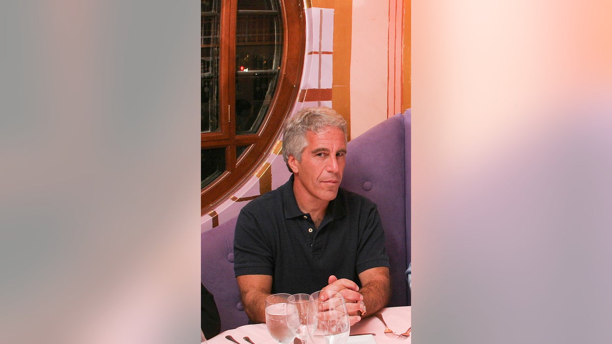 Jeffrey Epstein sitzt an einem Esstisch und trägt ein schwarzes Poloshirt