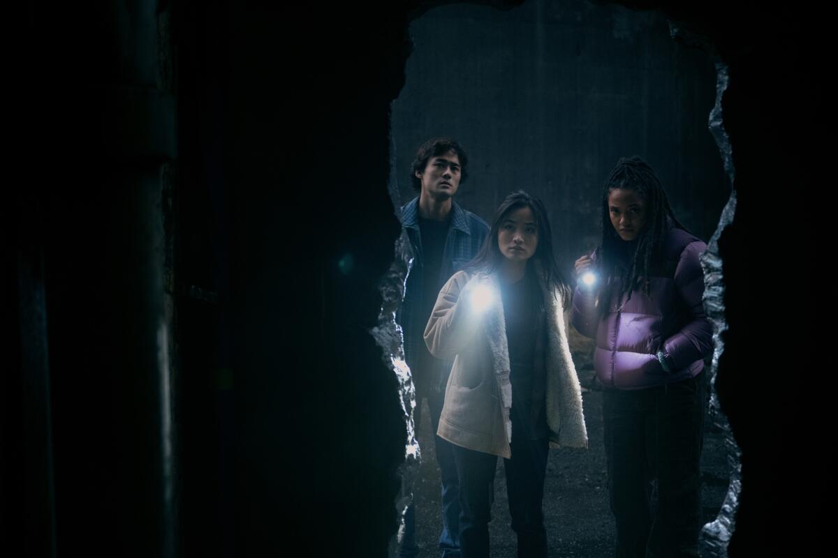 Ren Watabe, Anna Sawai und Kiersey Clemons blicken mit Taschenlampen in ein Loch in einer Wand