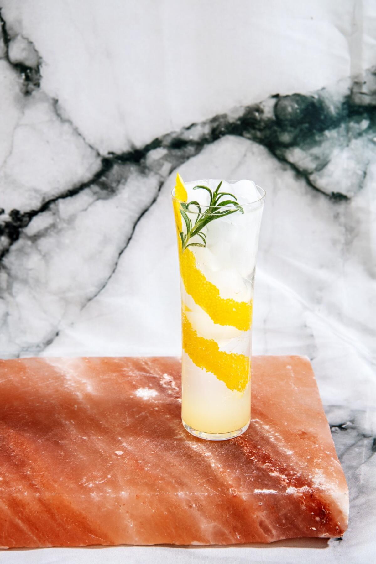 Yuzu-Spritzer in einem hohen Glas, garniert mit einem Streifen Zitronenschale und einem Rosmarinzweig