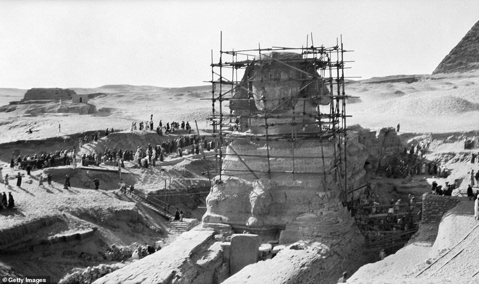 The Great Sphinx of Giza is encased in wooden scaffolding as dozens of workers go about excavating it in 1931