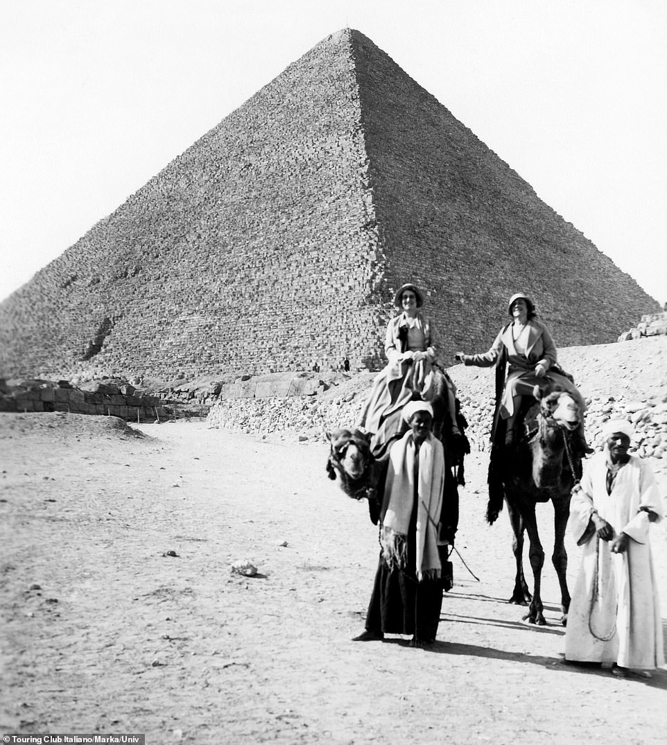 Two women smile for the camera as the embark on a tour of the Giza pyramids by camel in 1920. There doesn't appear to any other tourists around, as they traverse the dusty routes