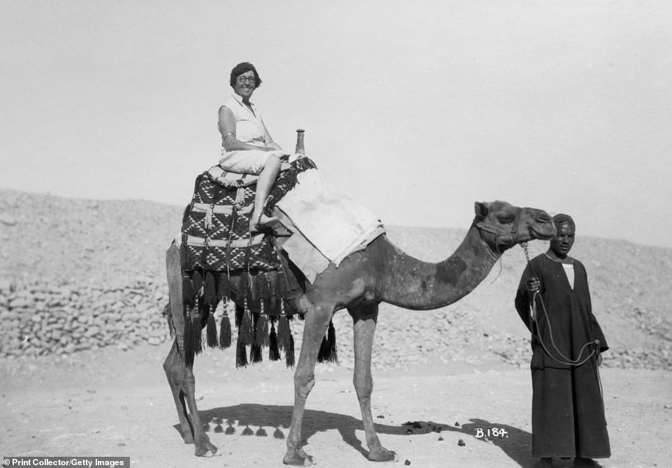 A tourist braves the heat in a white ensemble and heels while sitting atop a camel attended to by a local. The vacation photo was taken circa 1920, just as tourism started to flourish