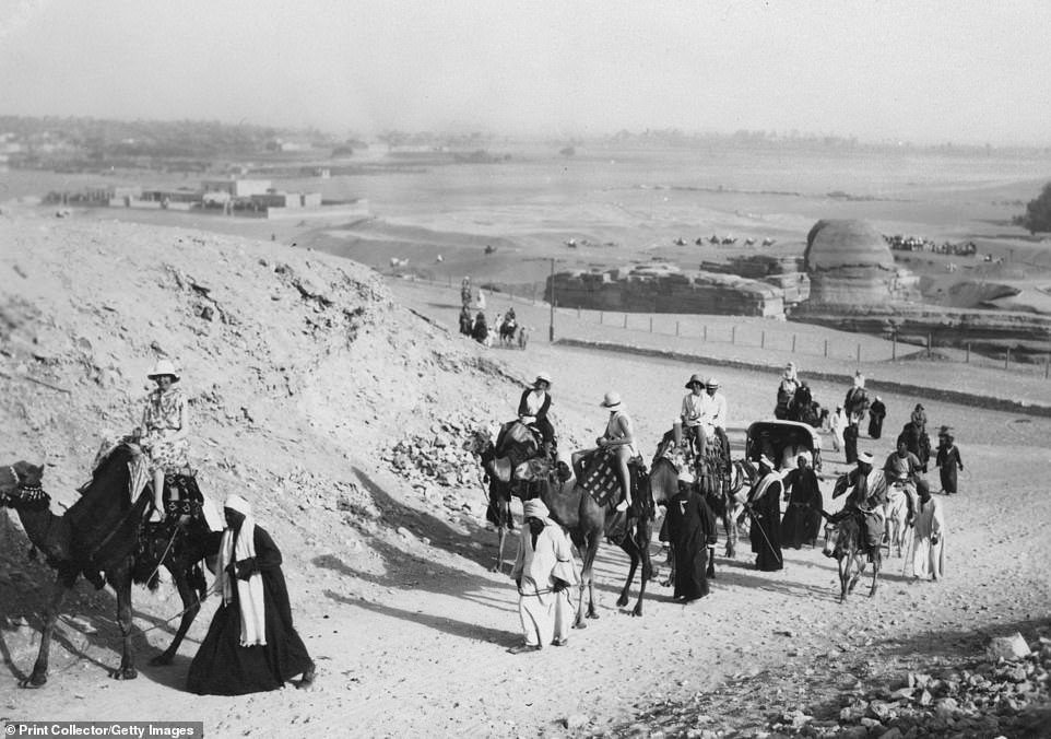 A group of tourists set off on a camel tour of Giza, with a horse and cab also in tow. The head of the Great Sphinx can be seen in the background on the right