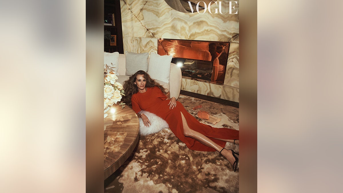Auf einem Bild für die britische Vogue liegt Julia Roberts in einem dunkelorangefarbenen Kleid mit Schlitz auf dem Boden gegen eine Couch