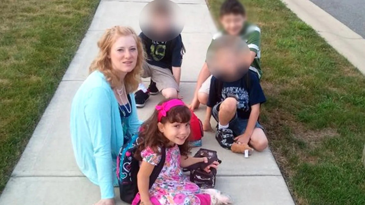 Kristine Barnett trägt einen leuchtend blauen Pullover und sitzt mit ihren Kindern auf dem Bürgersteig