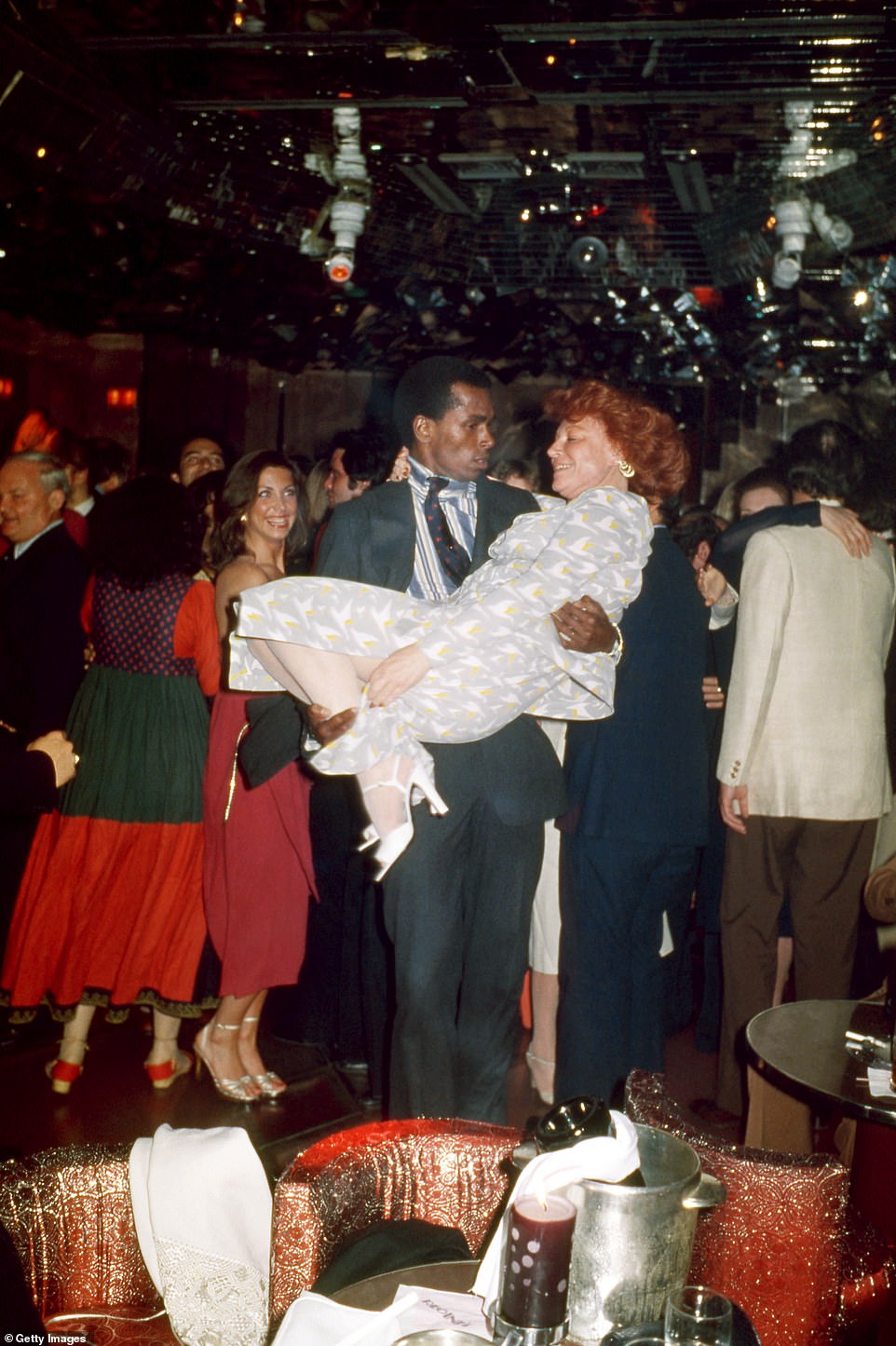 A rare color photo of St Jacques enjoying the sumptuous surroundings of Studio 54 in 1977 - with two women clearly delighted to be in his orbit. He is seen carrying French singer Régine Zylberberg, who passed in 2022, while an unidentified woman in red stood behind observes proceedings with evident glee