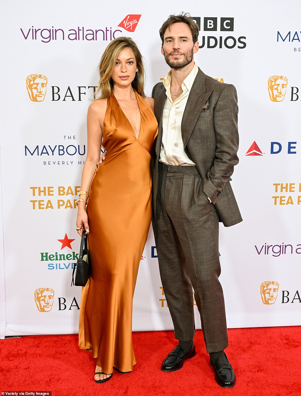 Cassie Amato donned a satin gold dress while Sam Claflin opted for a stylish, dark brown suit as they attended the event