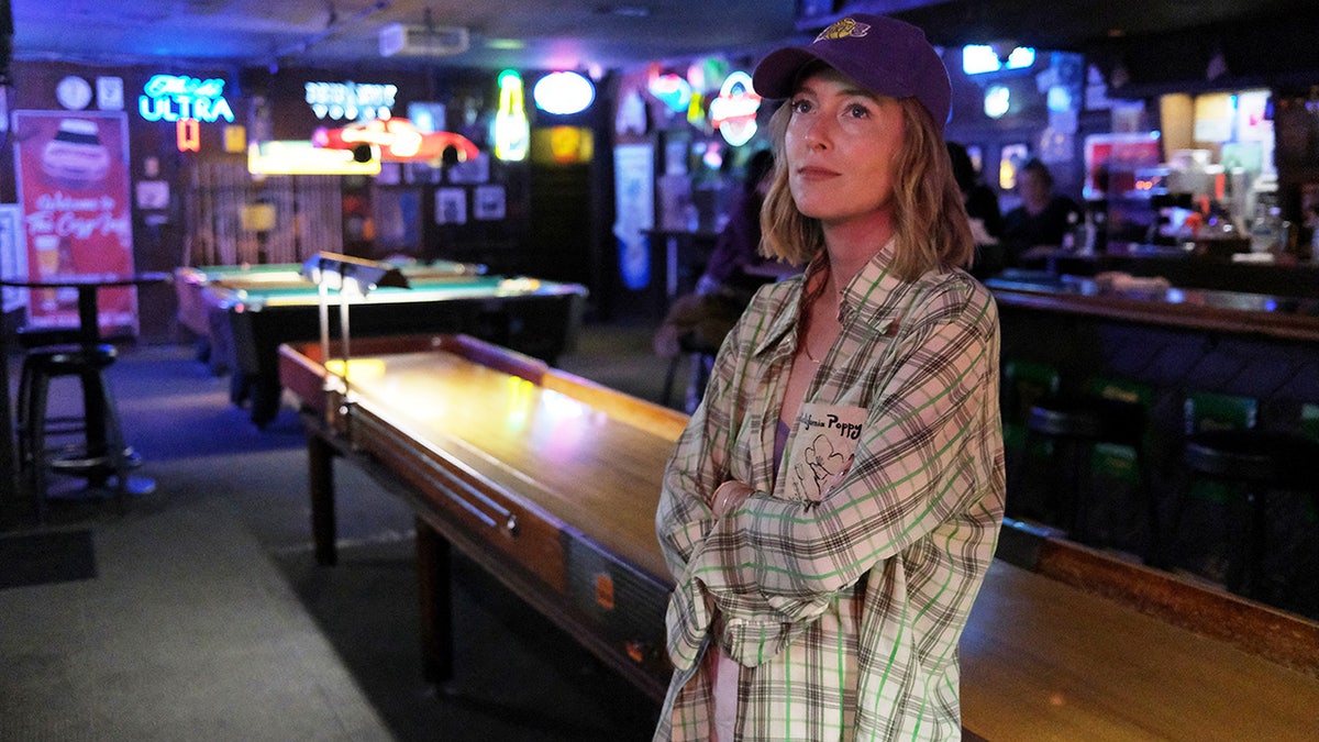 India Oxenberg trägt ein kariertes Hemd und einen Hut in einer Bar