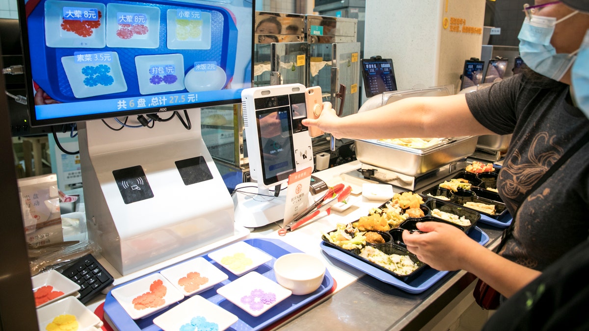Frau bezahlt Essen in der Cafeteria mit Smartphone