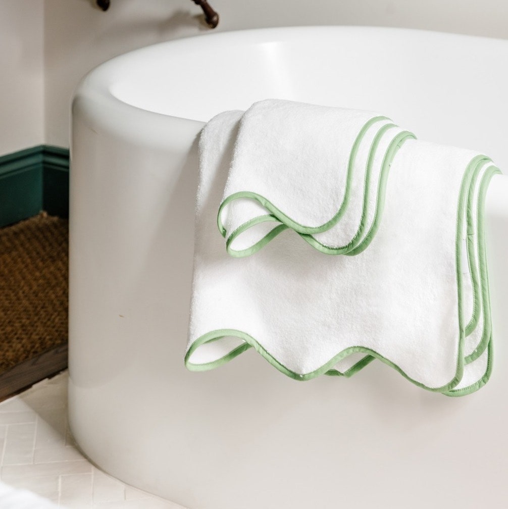 Weiße Handtücher mit grünem Wellenrand über einer weißen Wanne. 