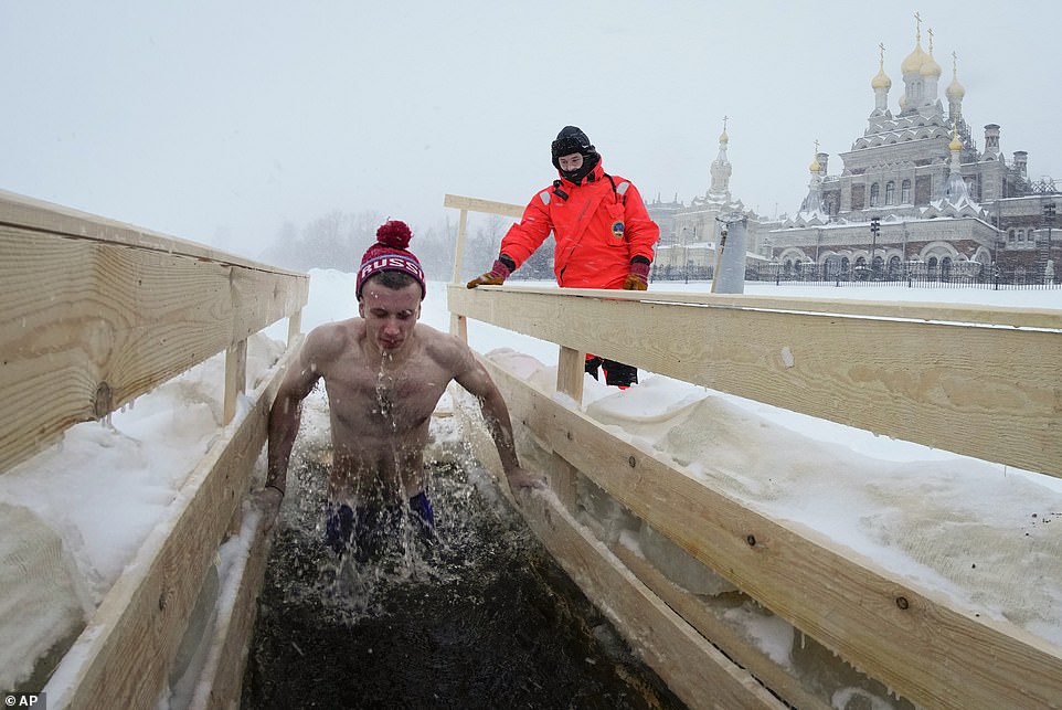 A rescue worker observes a Russian Orthodox believer dipping in the icy water in the Neva River during a traditional Epiphany celebration in St. Petersburg, Russia, on Thursday