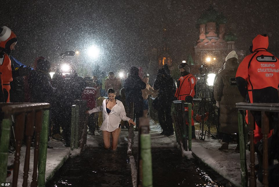 A young woman bathes into the icy water on Epiphany during a traditional Epiphany at the Great Palace Pond with the Church of the Holy Trinity in Ostankino in the background in Moscow, Russia, on Thursday night