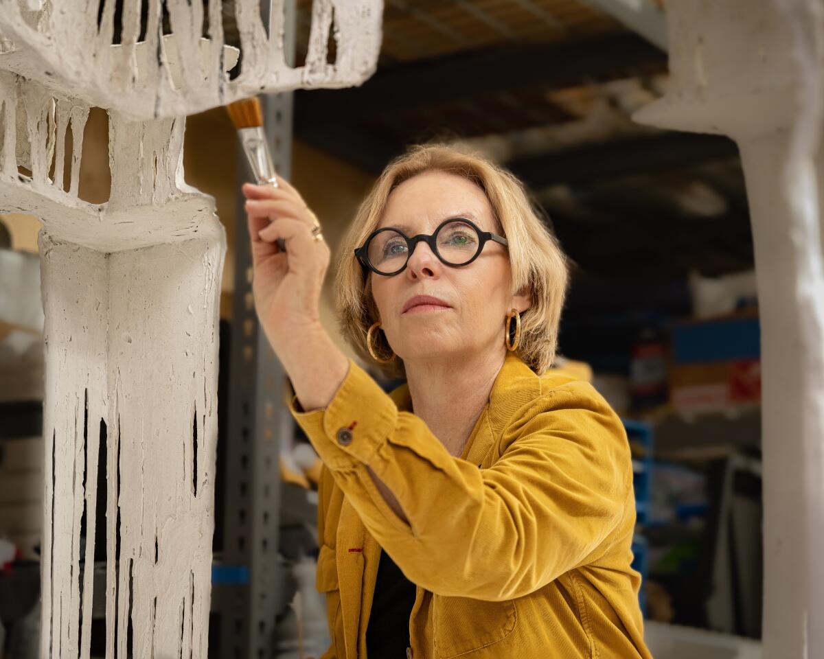Rosa Lowinger, eine Kunstrestauratorin und Autorin in einem senffarbenen Hemd, hält einen Pinsel an ein altes Werk, das sie restauriert.