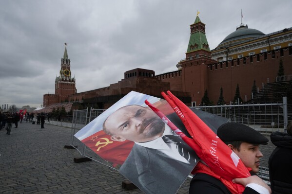 Russische Kommunisten tragen ein Porträt von Wladimir Lenin, dem Gründer der Sowjetunion, und rote Fahnen, nachdem sie am Freitag, dem 22. April 2022, sein Mausoleum anlässlich seines 152. Geburtstags auf dem Roten Platz in Moskau, Russland, besucht haben. (AP Photo/ Alexander Zemlianichenko, Akte)