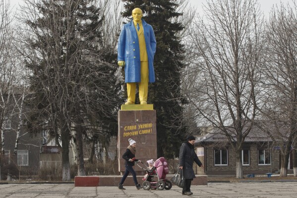   Menschen gehen am Donnerstag, 19. Februar 2015, in Welyka Nowosilka, Ukraine, an einer Statue von Wladimir Lenin vorbei, die in den Farben der ukrainischen Nationalflagge bemalt ist. (AP Photo/Vadim Ghirda, Datei)