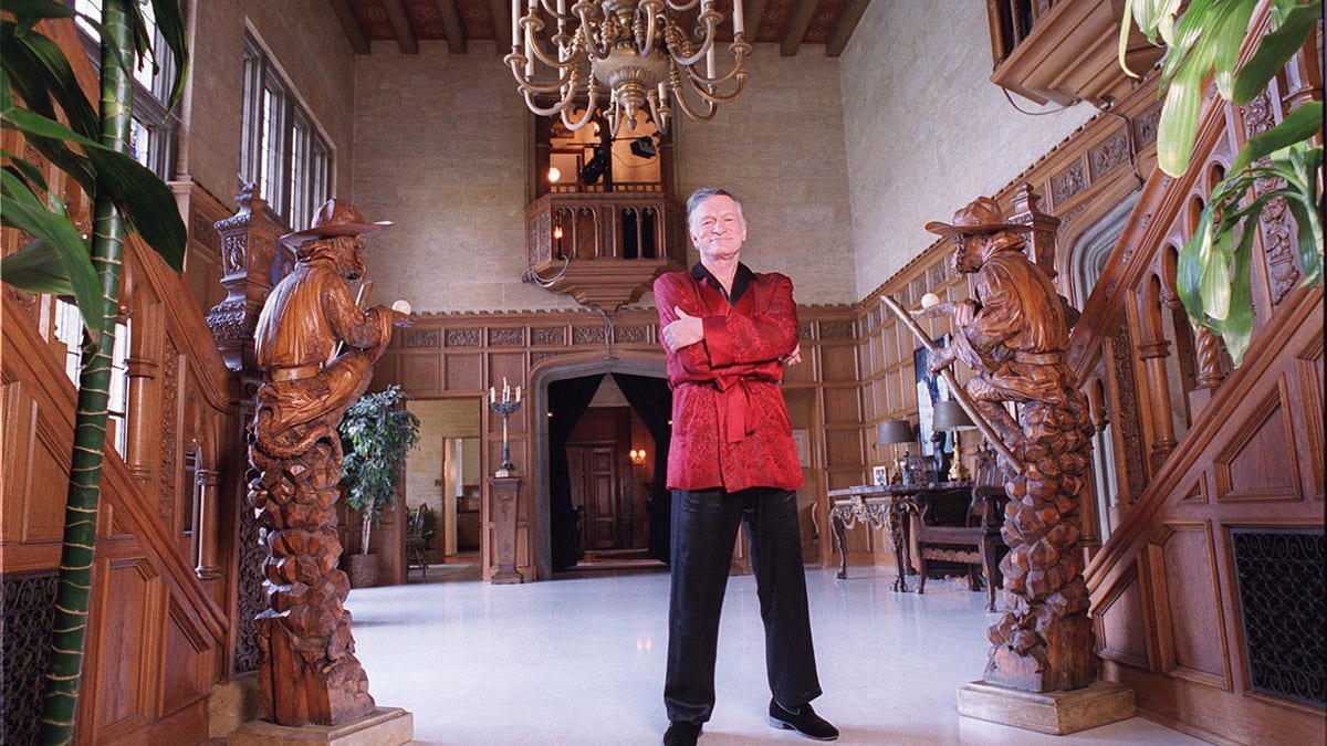 Hugh Hefner mit verschränkten Armen und einem roten Gewand in der Playboy Mansion