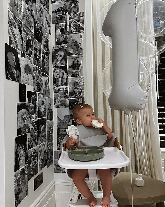 Bambi saß in einem Türsteher neben einer Fotowand, die mit Schwarz-Weiß-Bildern der Familie dekoriert war.  Es gab auch einen „Eins“-Ballon, der ihren ersten Geburtstag symbolisierte