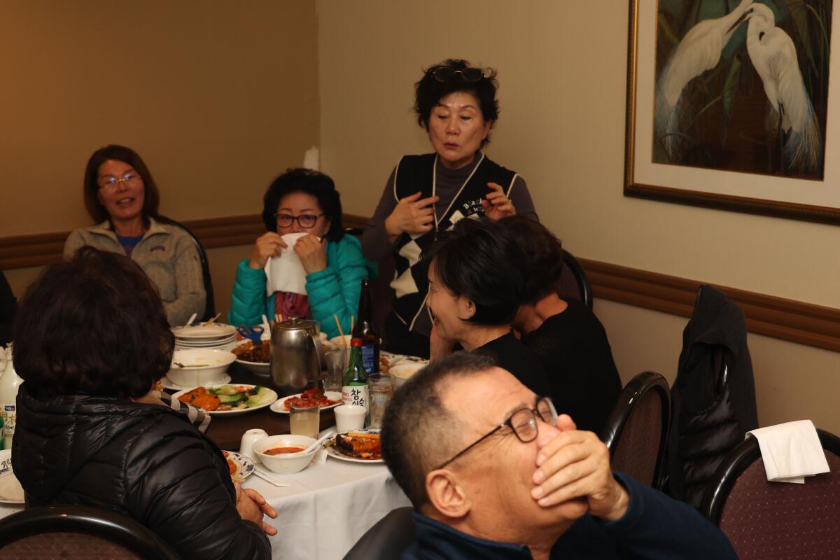 Eine Frau steht an einem Restauranttisch, während die sitzenden Gäste lachen