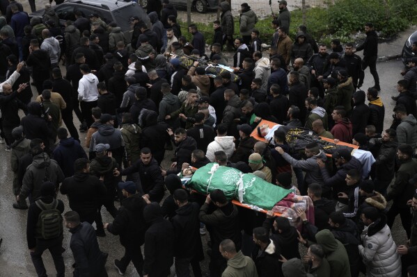 Palästinensische bewaffnete Männer marschieren mit Körpern von Militanten, die in die Flagge der militanten Hamas-Gruppe (links) und den Palästinensischen Islamischen Dschihad (rechts) gehüllt sind und bei einem israelischen Militärangriff auf das Ibn-Sina-Krankenhaus in der Stadt Dschenin im Westjordanland getötet wurden, Dienstag, 30. Januar 2024. (AP Photo/Majdi Mohammed)