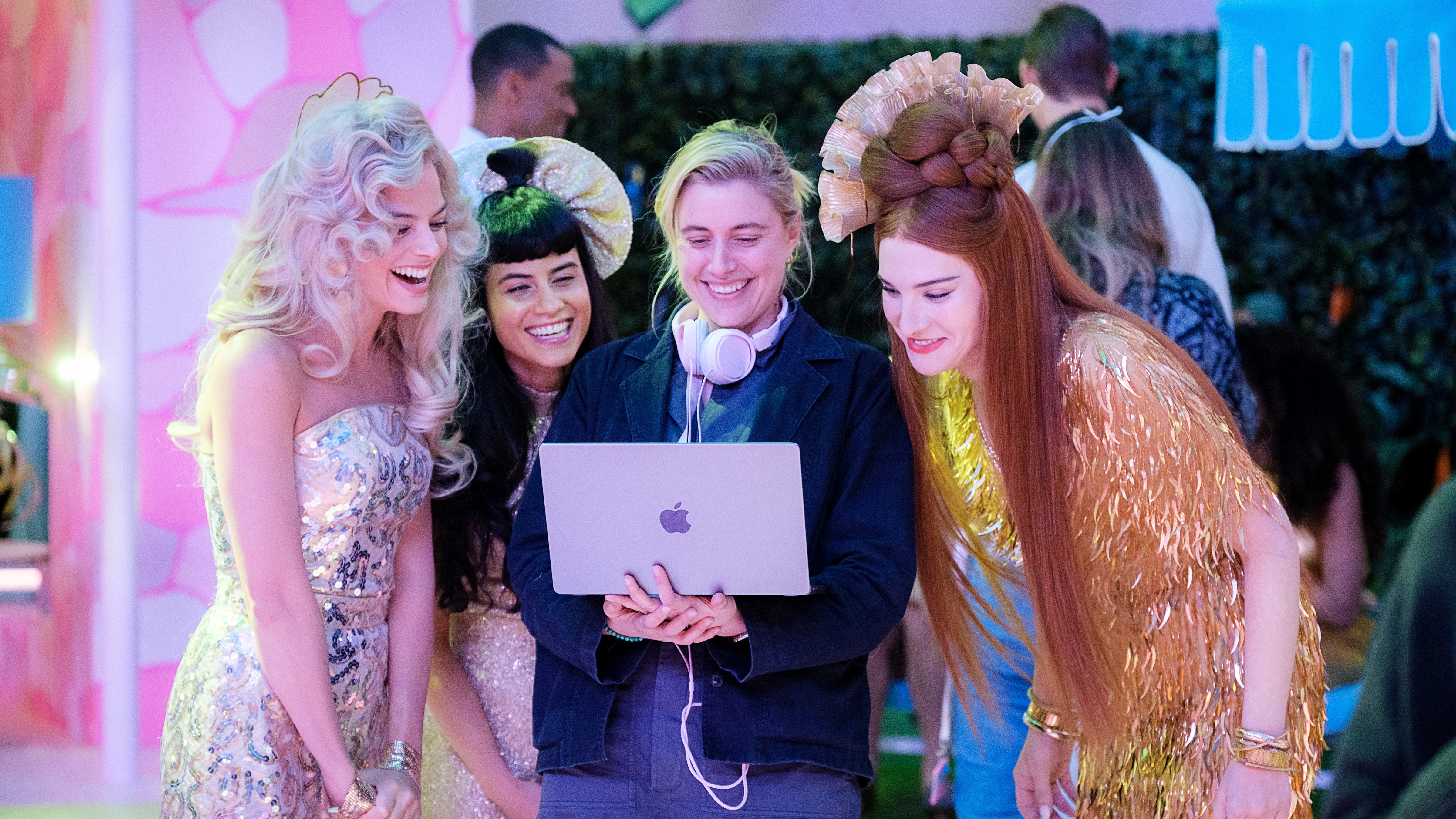 Ein Bild von Greta Gerwig am Set von Barbie, wie sie auf einen Laptop schaut, umgeben von Barbie-Stars (einschließlich Margot Robbie)