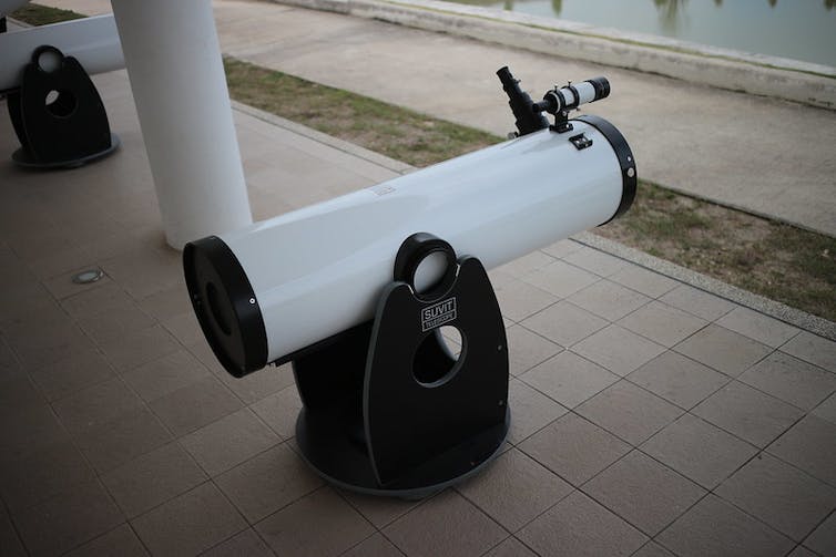 Ein weißes Teleskop auf schwarzem Sand auf einer gefliesten Veranda