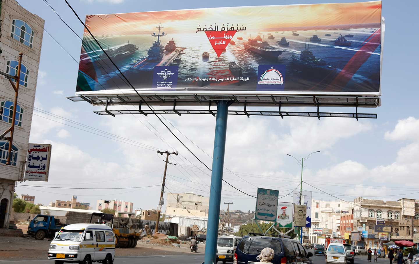 Jemeniten fahren am 31. Dezember 2023 auf einer Straße in Sana'a, Jemen, an einer Werbetafel vorbei, auf der die Marinezerstörer anderer Länder, darunter der USA und des Vereinigten Königreichs, und die Worte „Die Marinekoalition wird besiegt“ abgebildet sind.