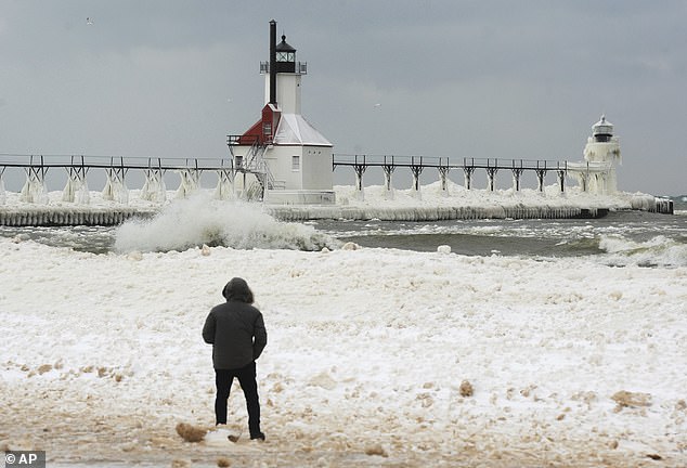 Schnee und Eis bedecken die St. Joseph Lighthouses in Michigan, während Wellen entlang des Lake Michigan-Schelfeises schlagen, das sich am Tiscornia Beach gebildet hat