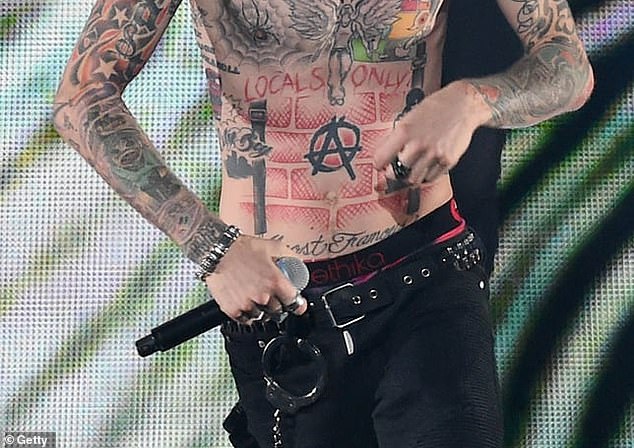 Eines der bemerkenswertesten Tattoos von MGK ist das Anarchy-„A“-Symbol in der Mitte seines Bauches.  Er wählte das Design, weil es eine „sehr starke Aussage“ über soziale Reformen sei