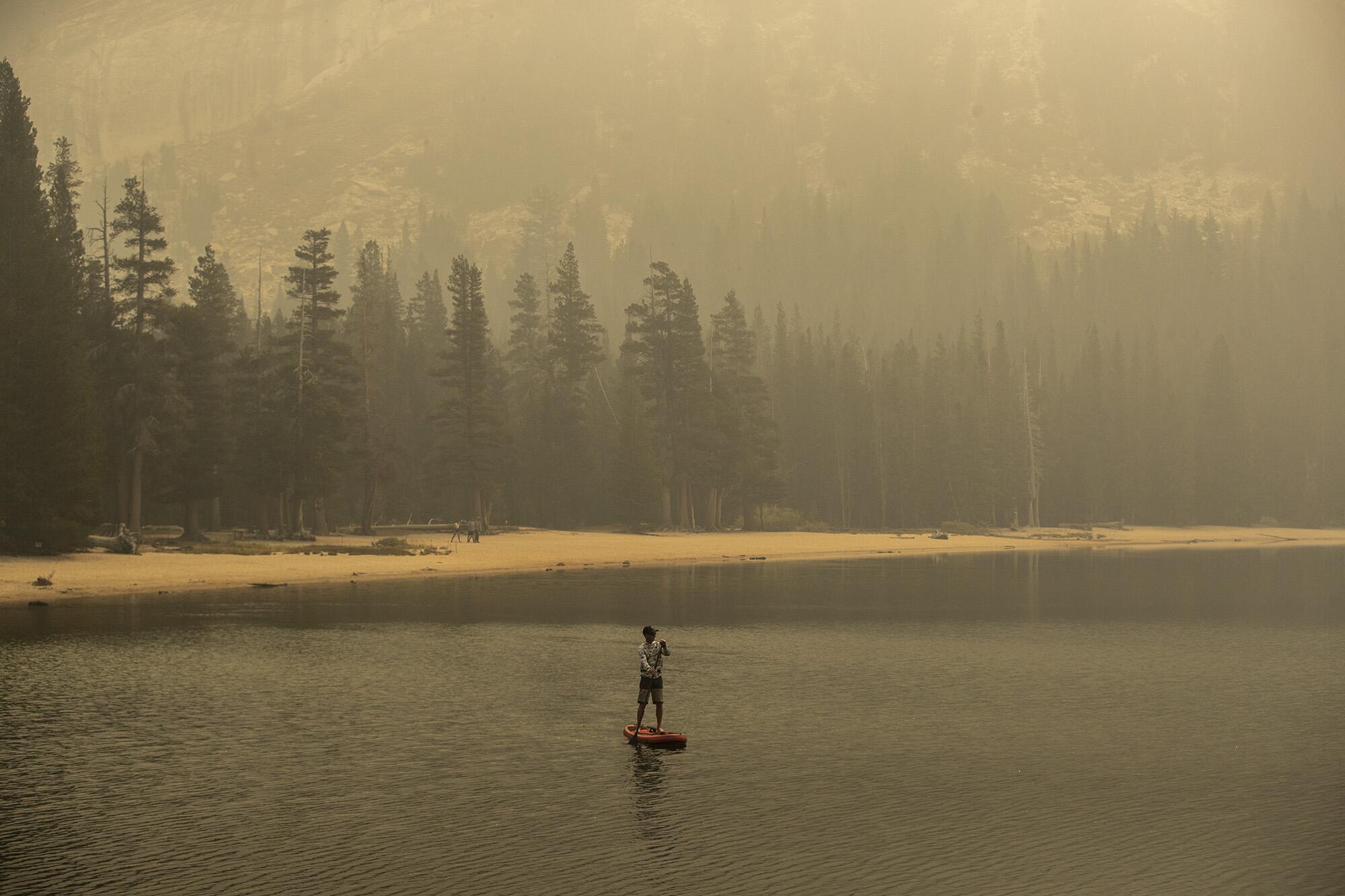 Eine einsame Figur paddelt auf einem rauchverhangenen See.